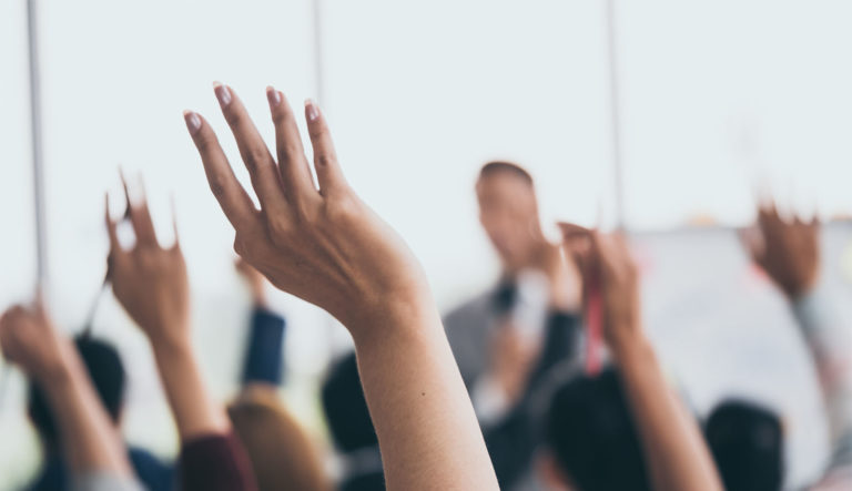 Audience raising hands up while businessman is speaking in training at the office.